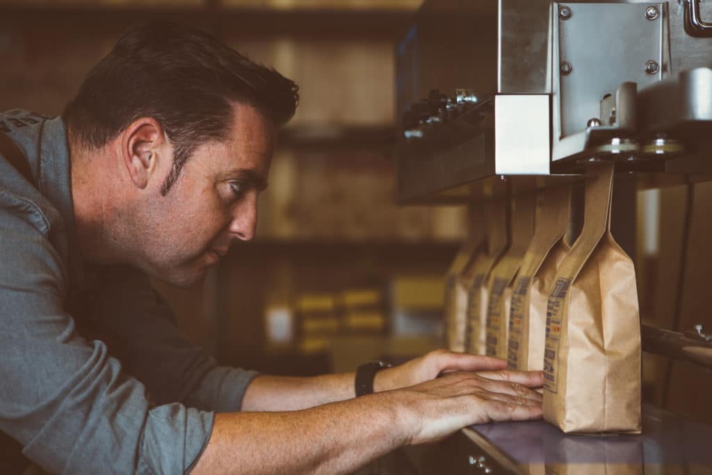 Side view of adult man looking at row of packages of roasted beans